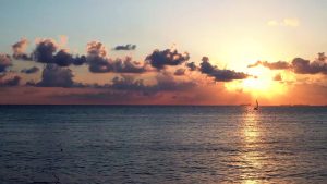 sunset over the ocean with sailboat